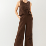Woman wearing a brown sleeveless top and wide-leg pants with floral embroidery on a white background