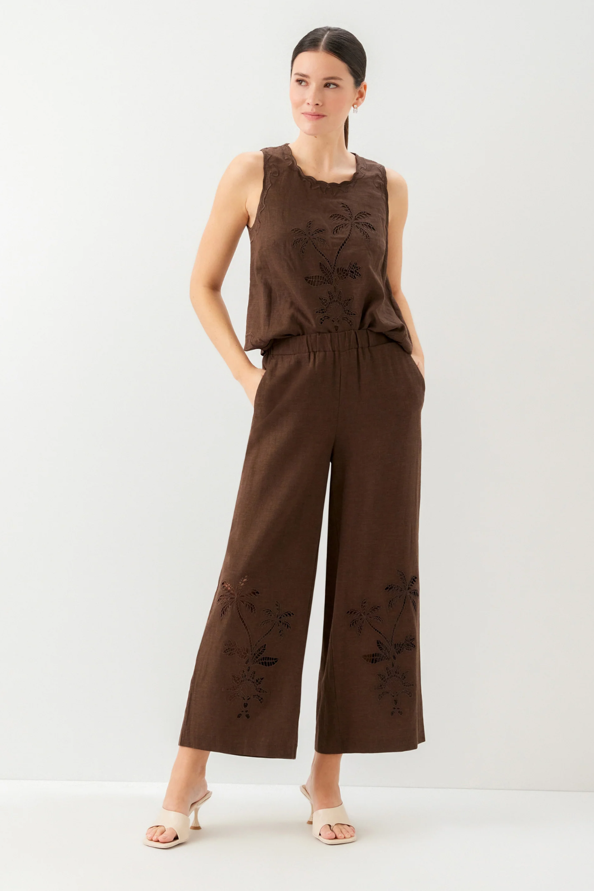 Woman wearing a brown sleeveless top and wide-leg pants with floral embroidery on a white background