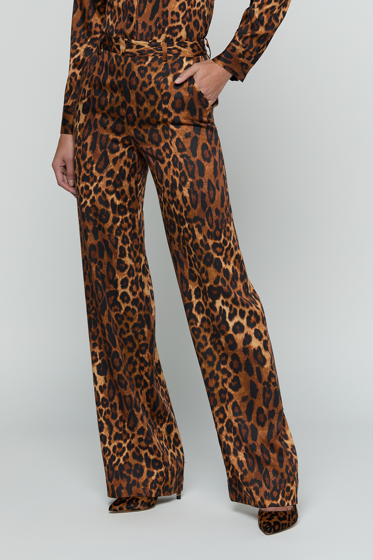 A model wearing a brown and black leopard print jumpsuit with wide legs, shown from the waist down against a light gray studio background.