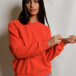 Woman wearing an orange sweater and blue jeans against a plain background