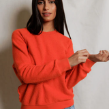 Woman wearing an orange sweater and blue jeans against a plain background