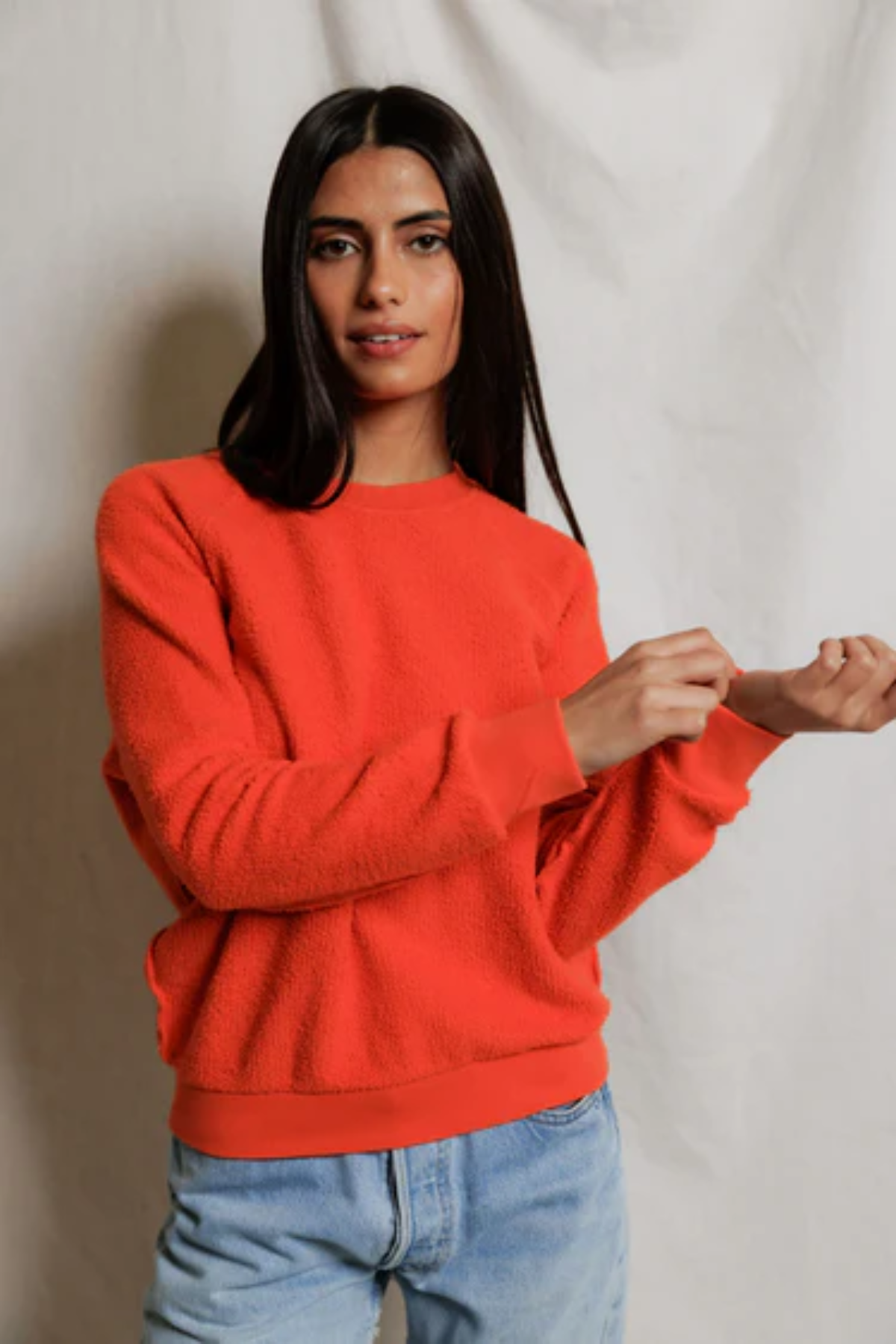 Woman wearing an orange sweater and blue jeans against a plain background