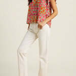 Woman wearing a colorful floral blouse and white pants on a plain background