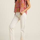 Woman wearing a colorful floral blouse and white pants on a plain background