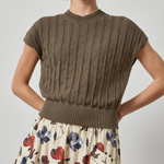 Woman wearing a brown knitted top and floral skirt on a plain background