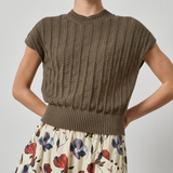 Woman wearing a brown knitted top and floral skirt on a plain background