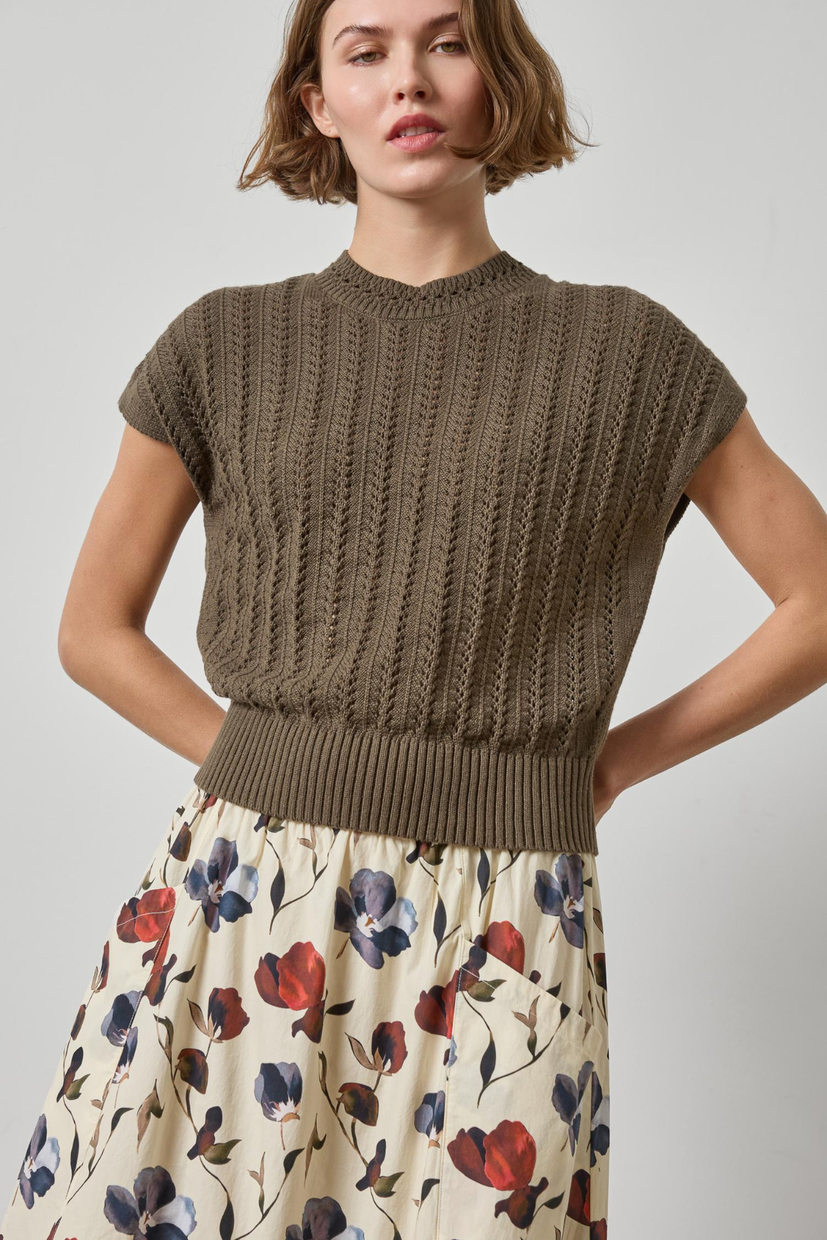Woman wearing a brown knitted top and floral skirt on a plain background