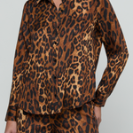 A model wearing a matching long-sleeve button-up shirt and trousers set in a brown and black leopard print fabric, shown against a plain light gray studio background.
