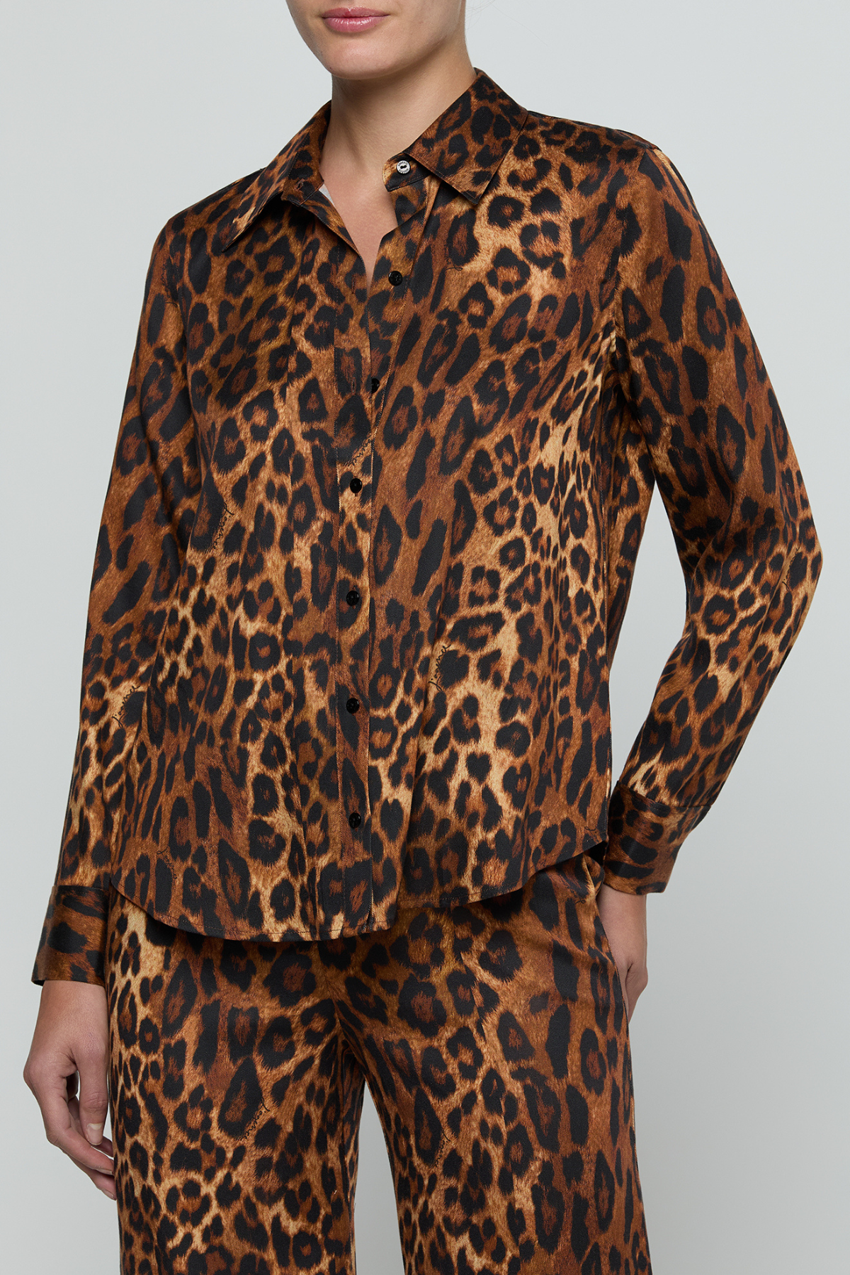 A model wearing a matching long-sleeve button-up shirt and trousers set in a brown and black leopard print fabric, shown against a plain light gray studio background.