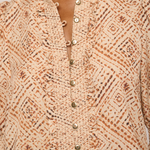 Close-up of a beige and brown patterned blouse with a ruffled collar and front button placket, worn by a model.