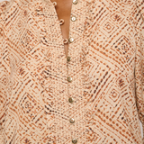 Close-up of a beige and brown patterned blouse with a ruffled collar and front button placket, worn by a model.