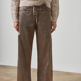 A model wearing a beige cable-knit sweater and brown wide-leg pants with a satin-like sheen, paired with white pointed-toe heels, set against a minimalist studio background.