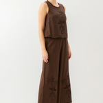 Woman wearing a brown sleeveless top and wide-leg pants with floral embroidery on a white background