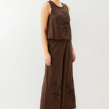Woman wearing a brown sleeveless top and wide-leg pants with floral embroidery on a white background