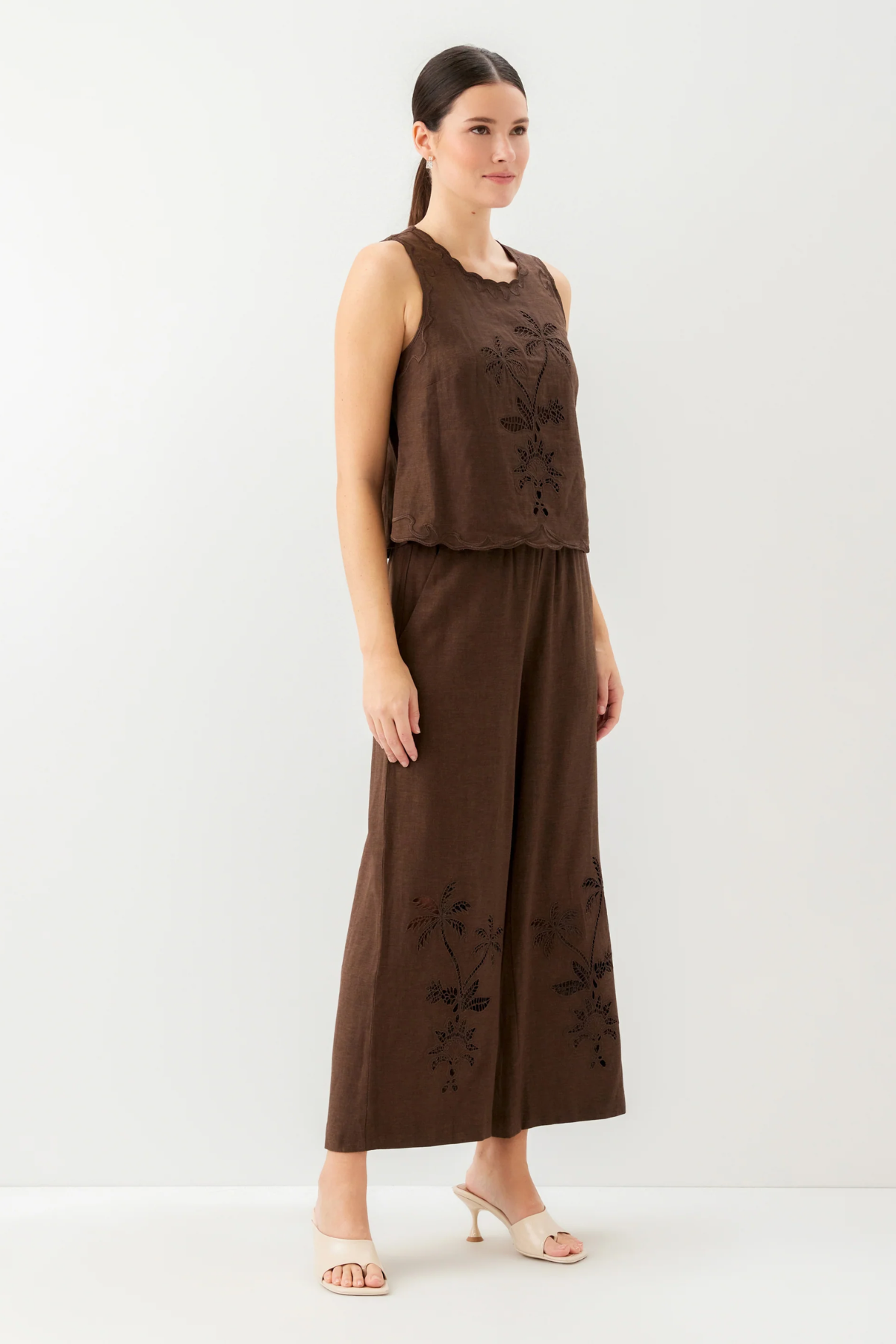Woman wearing a brown sleeveless top and wide-leg pants with floral embroidery on a white background