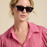 Woman wearing black sunglasses and a pink checkered shirt against a beige background