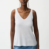 Woman wearing a white tank top and blue jeans on a plain background