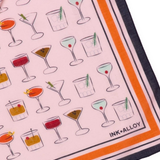 A close-up of a square scarf featuring a light pink background printed with various cocktail illustrations. The scarf has a bold orange stripe border, a dark navy blue border, and the brand name 'INK*ALLOY' printed in the bottom right corner.