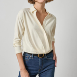 Woman wearing a cream blouse and blue jeans on a plain background
