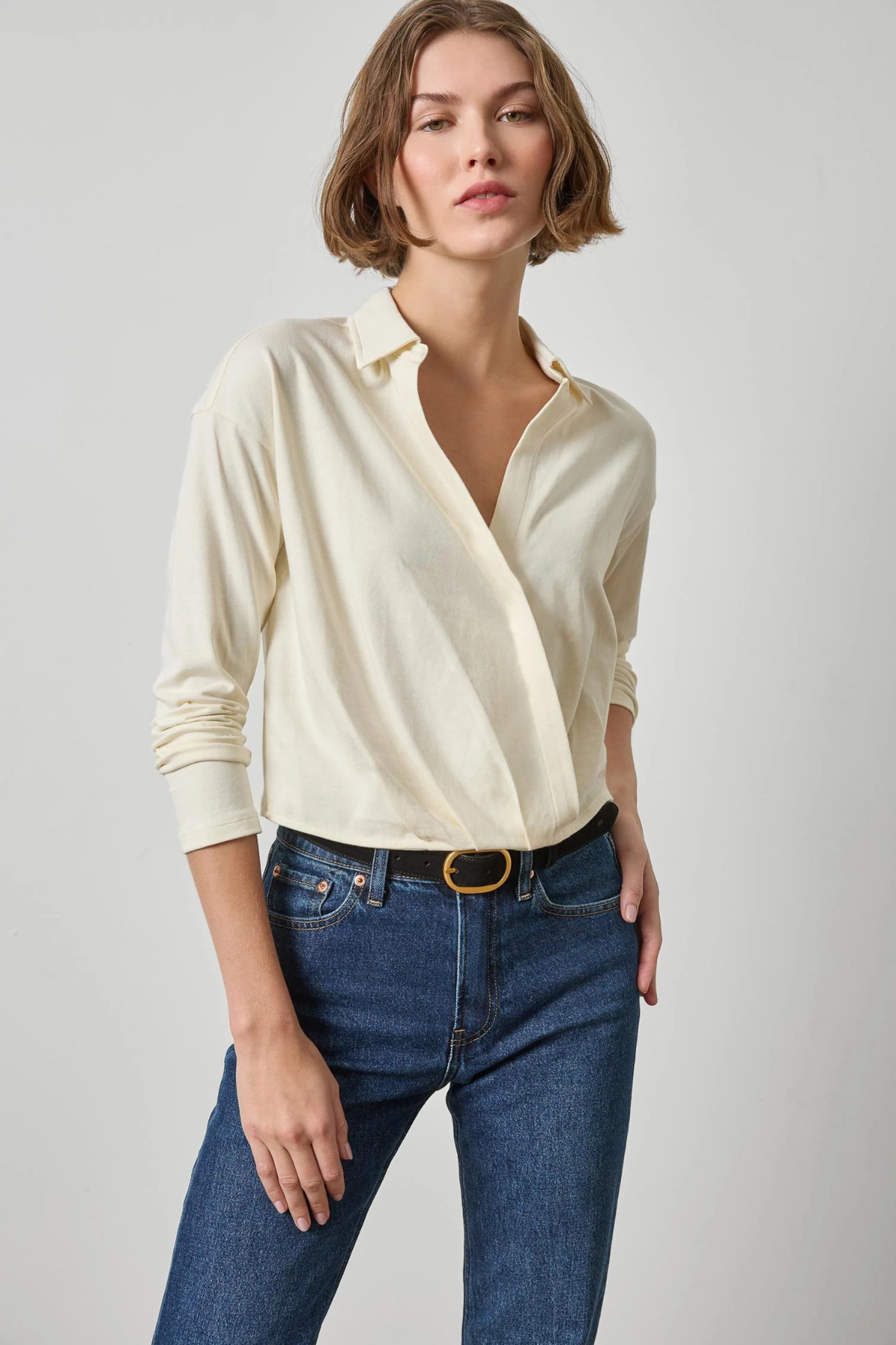 Woman wearing a cream blouse and blue jeans on a plain background