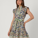 A woman modeling a short, sleeveless dress with a high mock neck, ruffled cap sleeves, and a matching tie belt at the waist. The dress features an intricate multicolor paisley pattern with green, blue, beige, and brown tones, set against a plain light gray studio background.