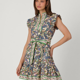 A woman modeling a short, sleeveless dress with a high mock neck, ruffled cap sleeves, and a matching tie belt at the waist. The dress features an intricate multicolor paisley pattern with green, blue, beige, and brown tones, set against a plain light gray studio background.