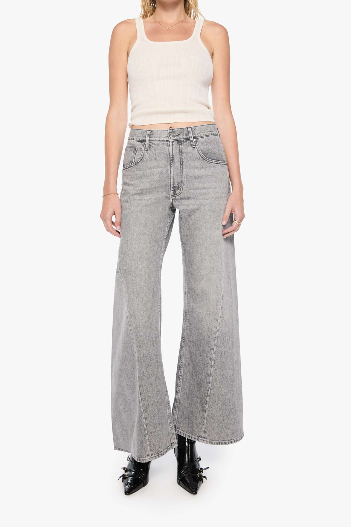 A model wearing light gray wide-leg denim jeans, a cream ribbed tank top, and black pointed-toe heels, standing against a plain white studio background.