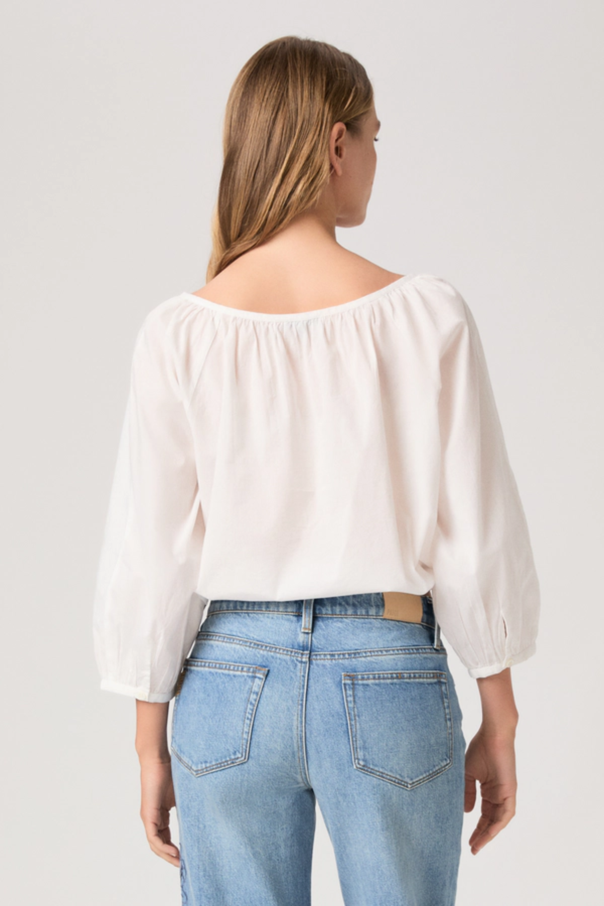 Woman wearing a white blouse and blue jeans on a plain background
