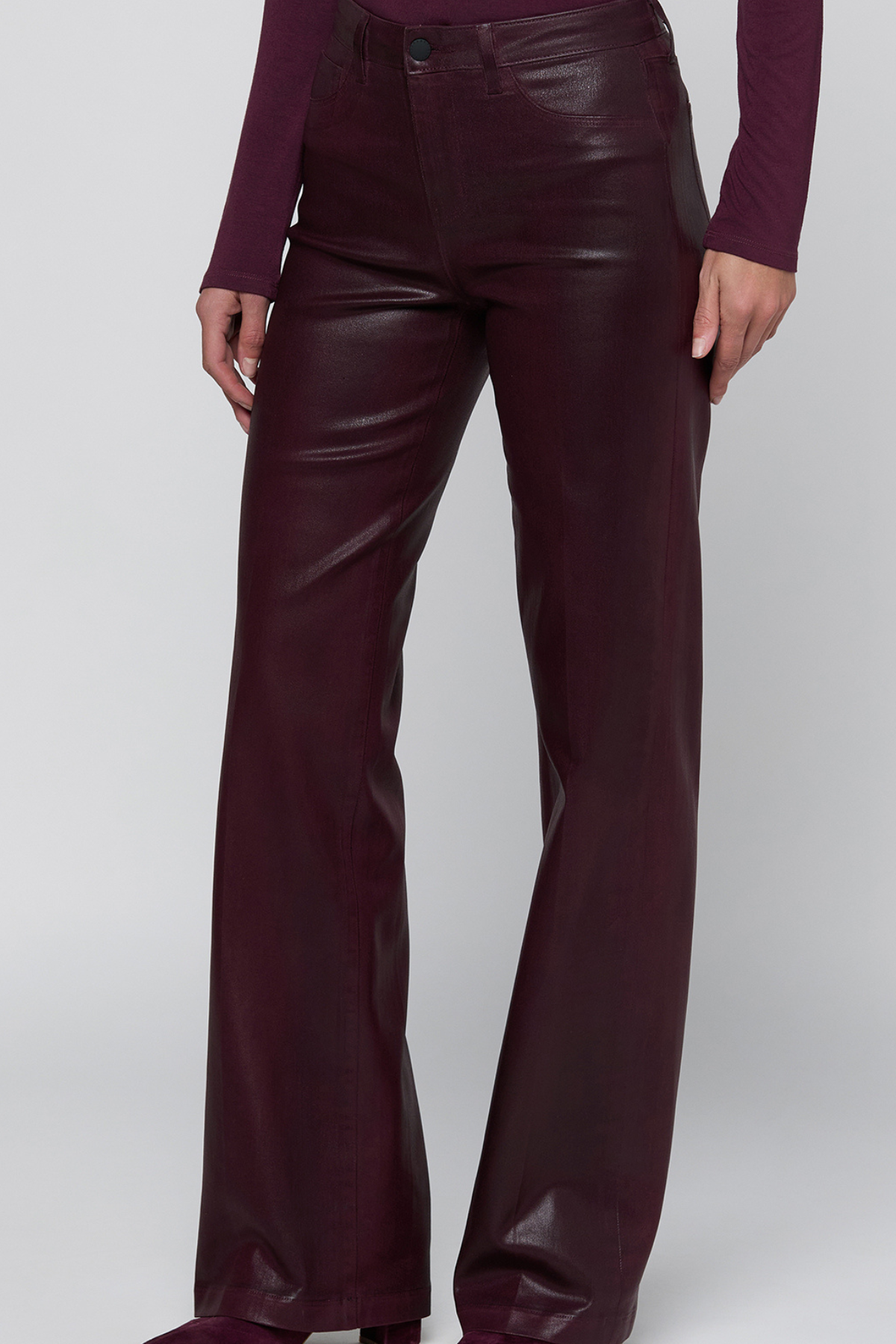 A person wearing high-waisted, wide-leg faux leather pants in a deep burgundy color, paired with a matching long-sleeve top, shown against a light gray studio background.