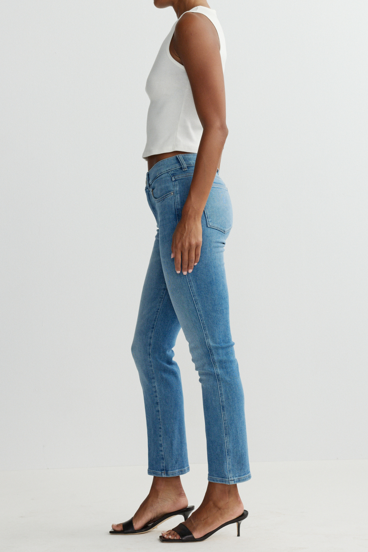 Person wearing light blue jeans and a white top on a plain background
