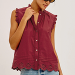 Woman wearing a burgundy sleeveless top with lace details and blue jeans on a white background