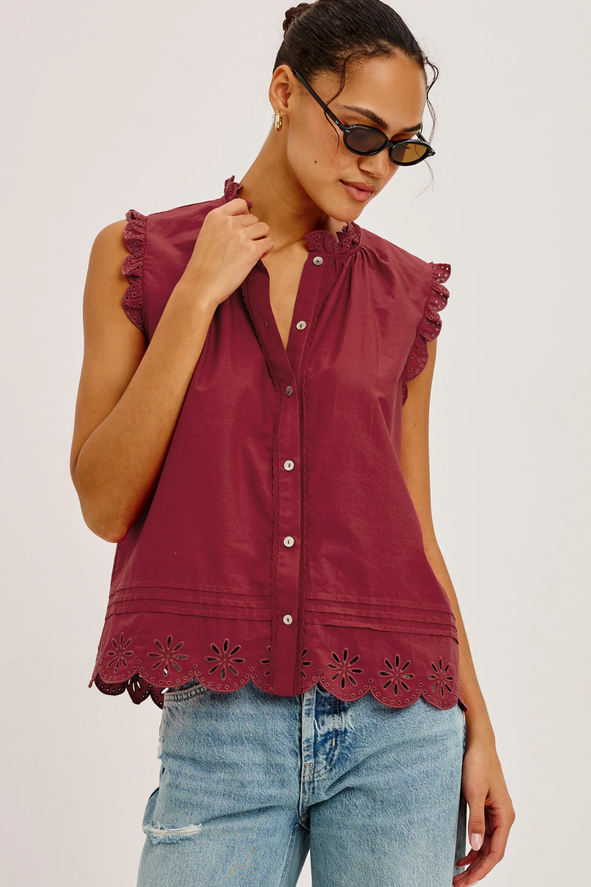 Woman wearing a burgundy sleeveless top with lace details and blue jeans on a white background