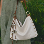 White handbag with brown straps and decorative elements held by a person wearing a green dress.