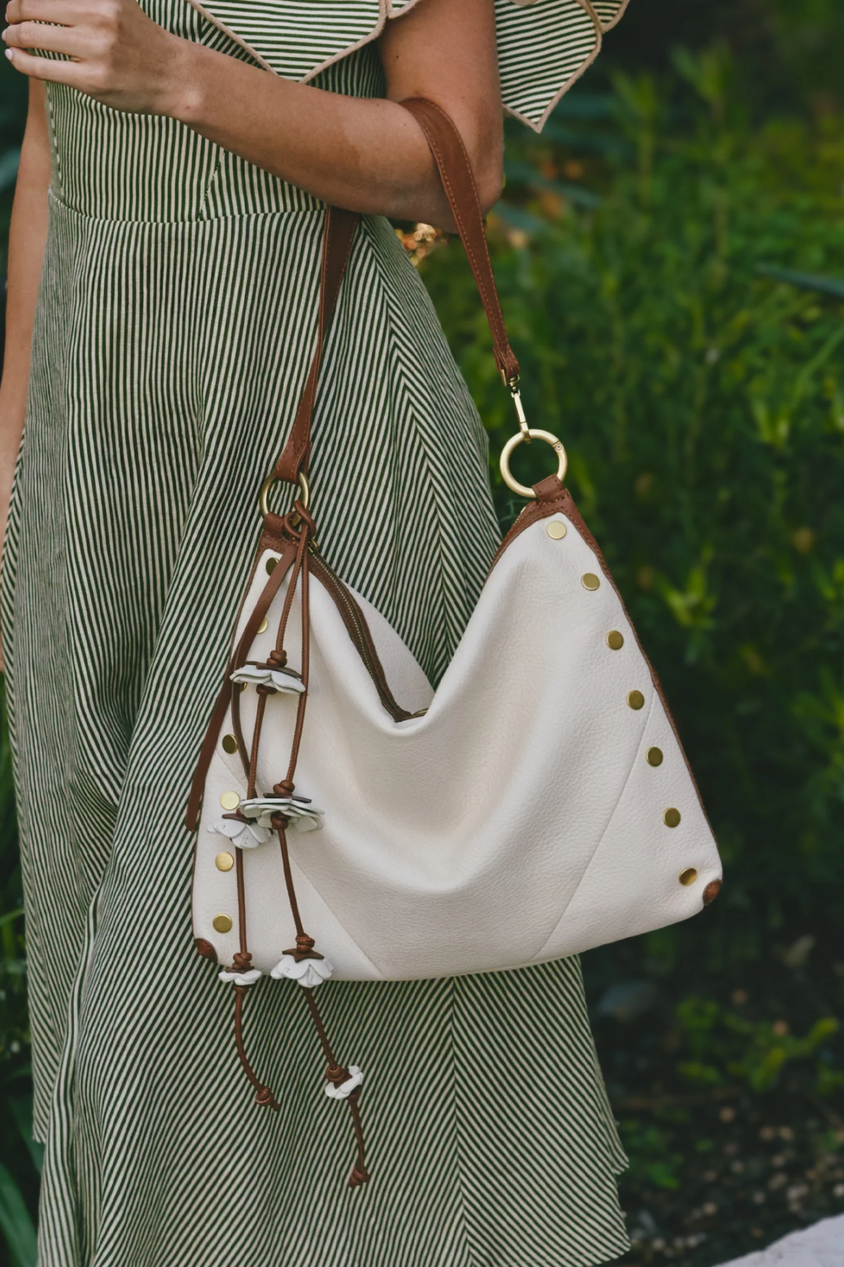 White handbag with brown straps and decorative elements held by a person wearing a green dress.