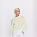 Person wearing a light green sweater and white pants on a white background