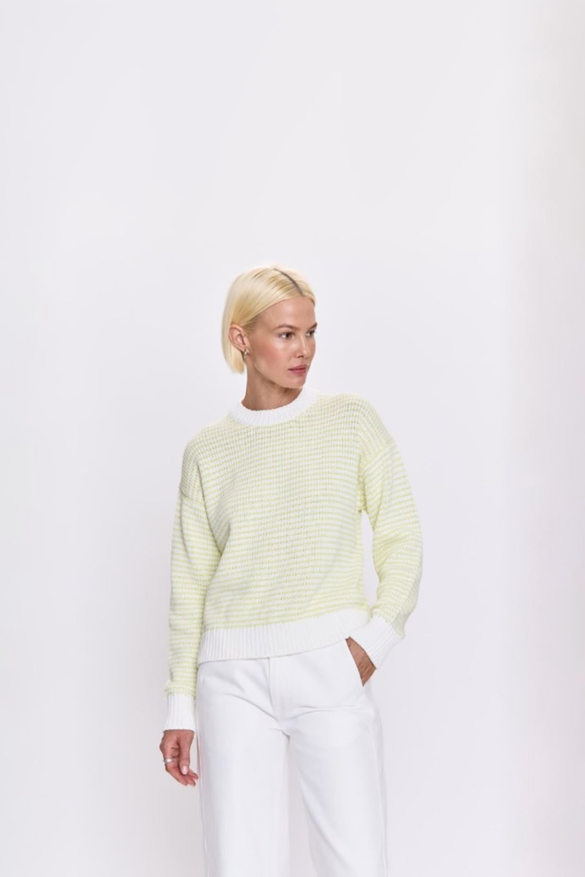 Person wearing a light green sweater and white pants on a white background