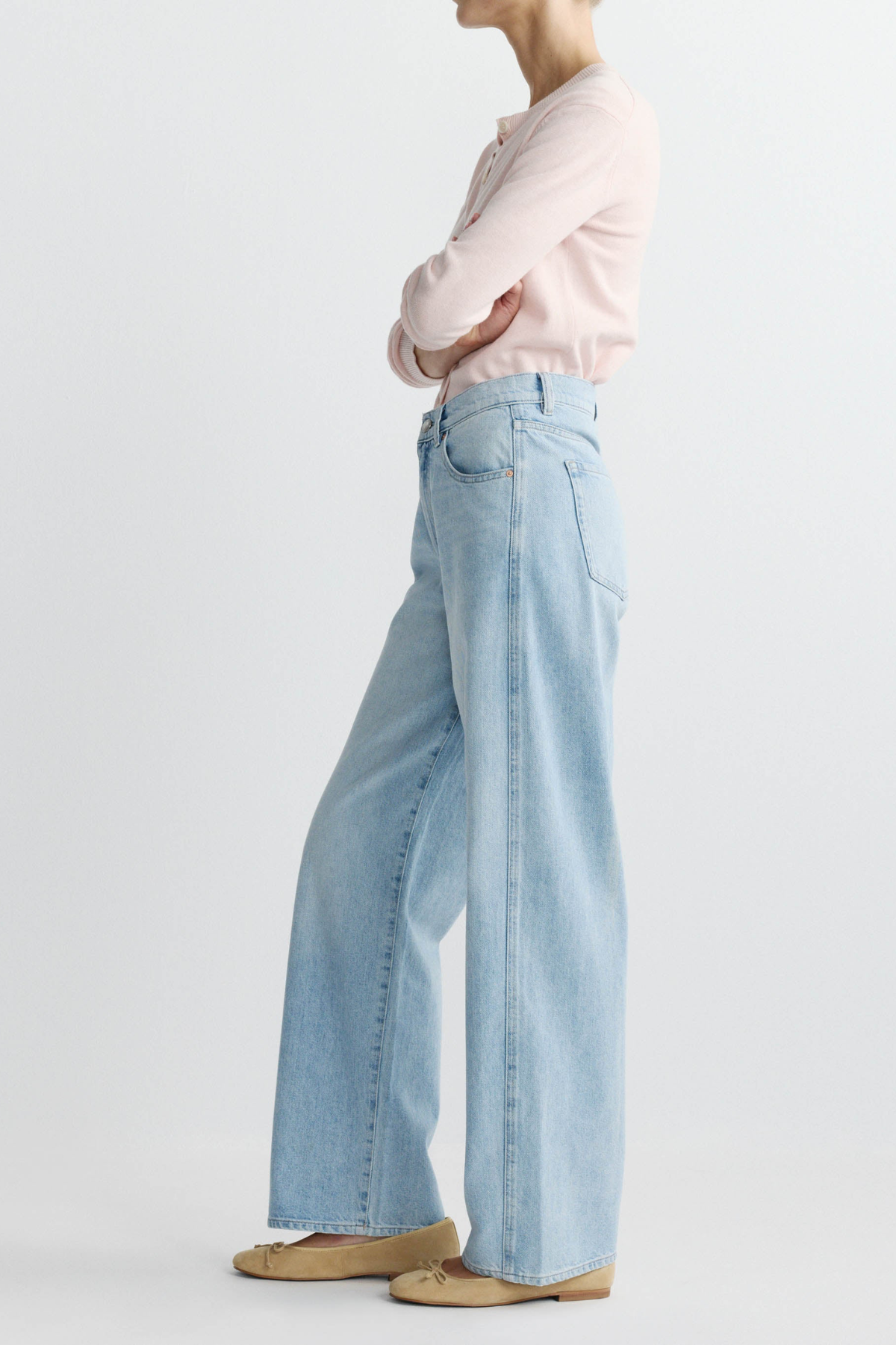 Person wearing light blue jeans and a pink shirt on a plain background