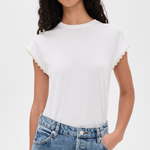 A woman wearing a white short-sleeve crewneck t-shirt with delicate scalloped edges on the sleeves, paired with light-wash blue jeans, against a plain white background.