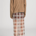 Person wearing a brown jacket and plaid skirt on a plain background