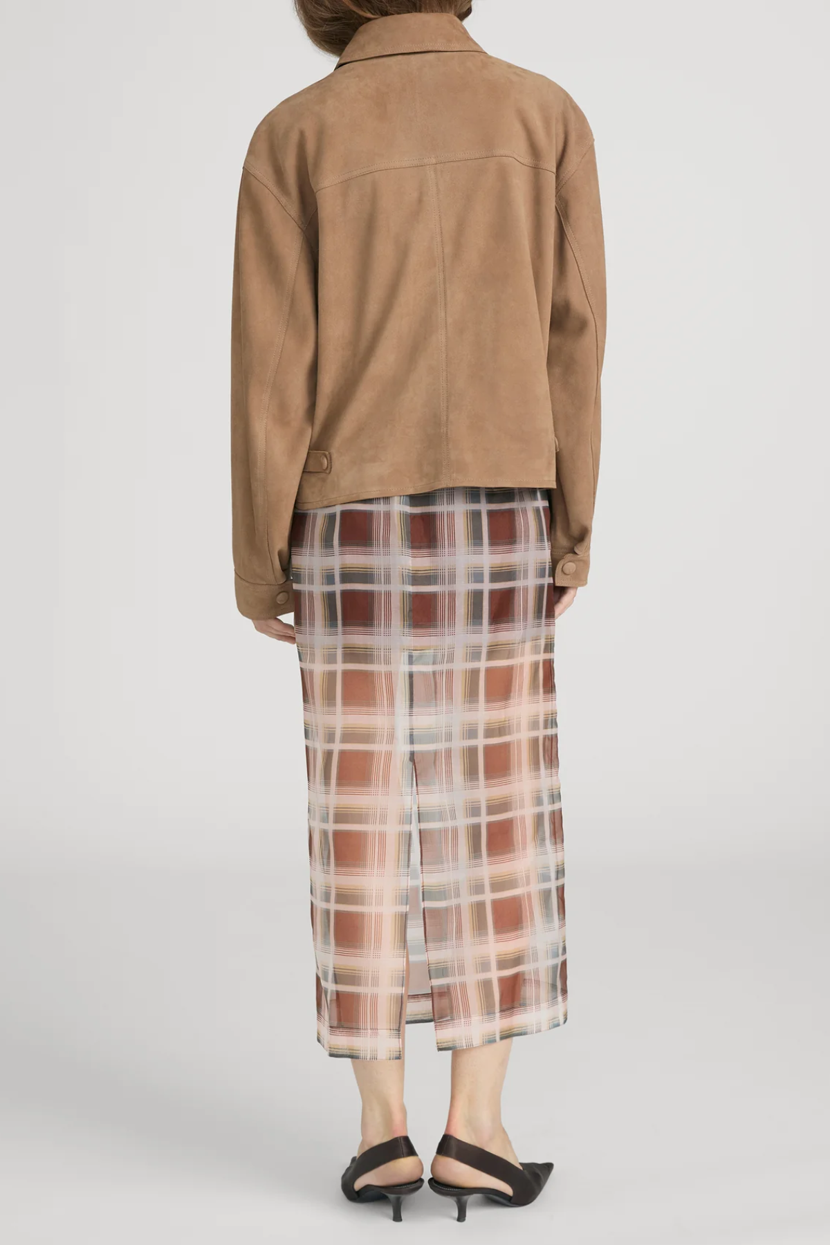 Person wearing a brown jacket and plaid skirt on a plain background