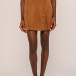 A model wearing a brown suede mini skirt with a matching belt and tie, paired with a matching brown top and brown pointed-toe flats, against a plain light background.