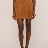 A model wearing a brown suede mini skirt with a matching belt and tie, paired with a matching brown top and brown pointed-toe flats, against a plain light background.