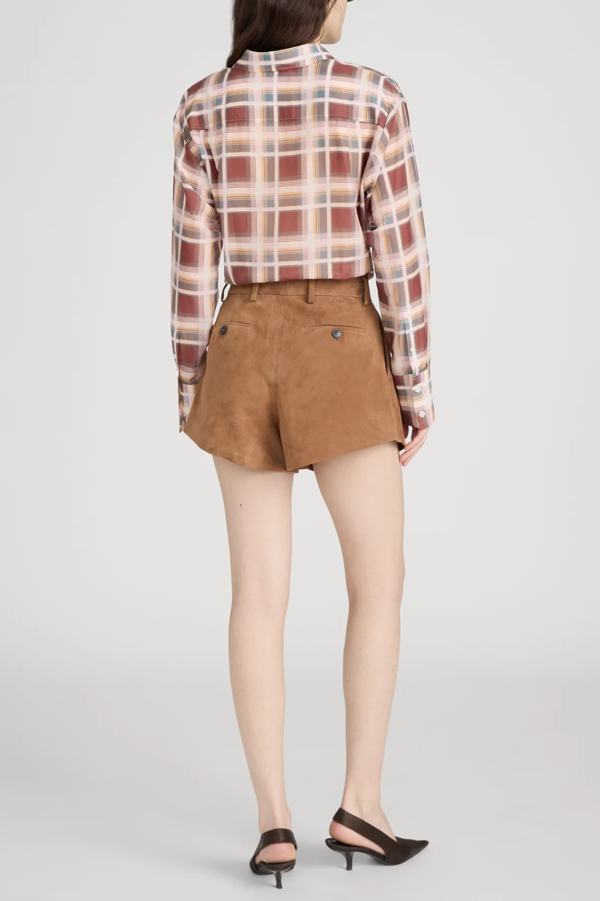 Person wearing a plaid shirt and brown shorts on a light gray background