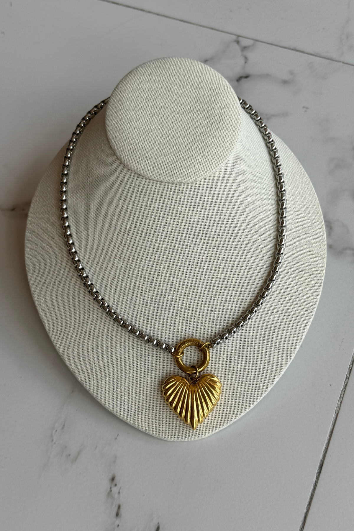 Mixed metal heart necklace on marble floor.