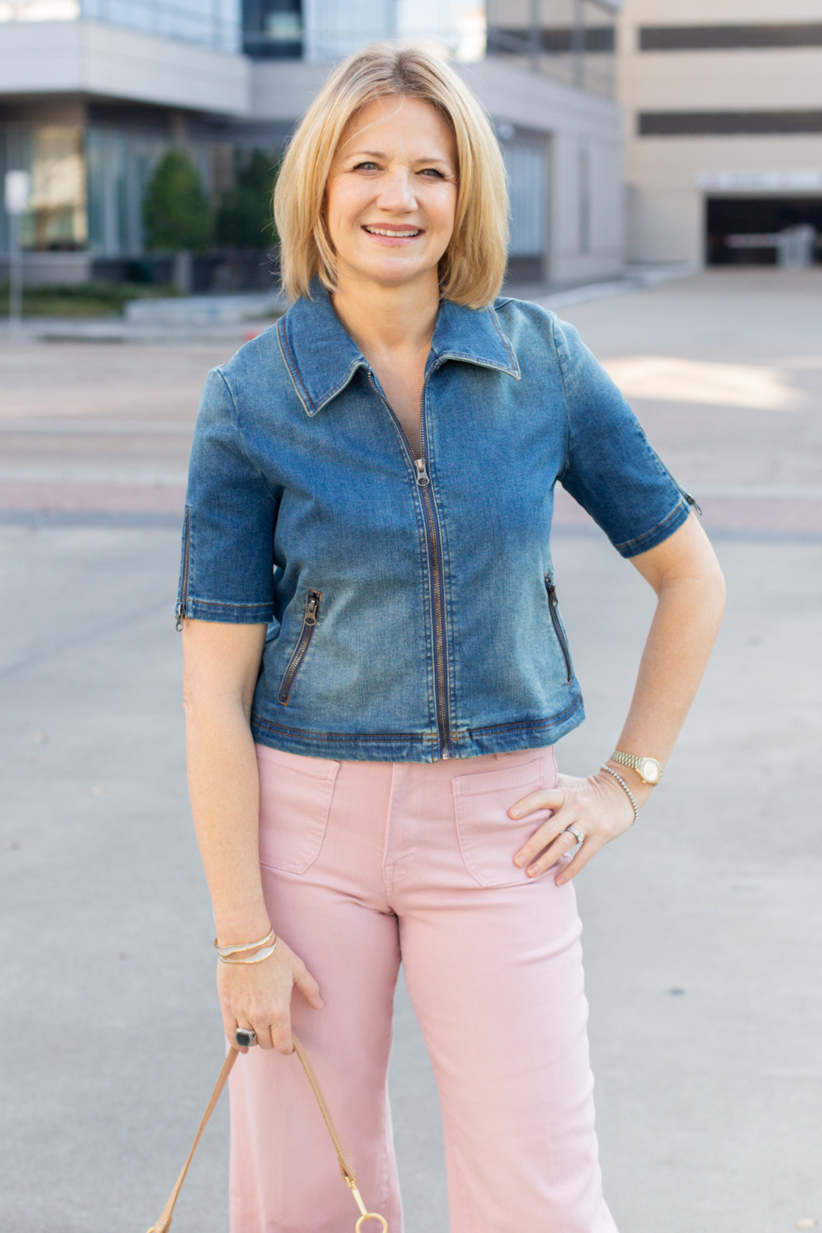 Woman wearing a denim jacket and pink pants standing outdoors.