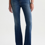 A model wearing a pair of dark blue high-waisted flare jeans with a subtle whiskering effect at the thighs, paired with a black top and black pointed-toe boots against a light gray studio background.