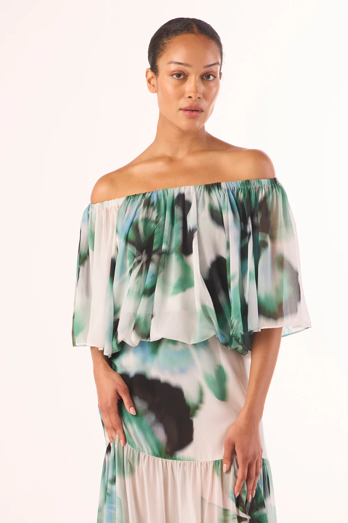 Woman wearing a green and white floral off-shoulder dress on a white background