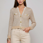 Woman wearing a beige knitted cardigan with gold buttons on a plain background