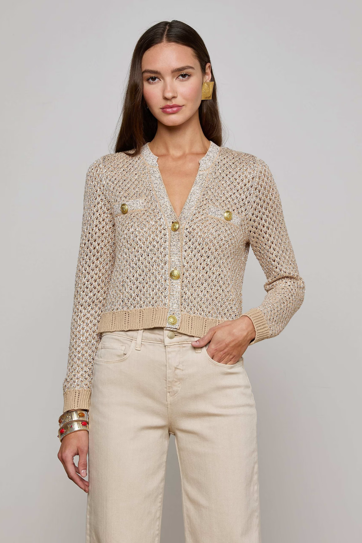 Woman wearing a beige knitted cardigan with gold buttons on a plain background