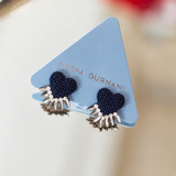 A pair of Deepa Gurnani stud earrings displayed on a light blue triangular card. The earrings feature dark navy blue seed bead hearts with silver-toned metal spikes extending from the bottom.